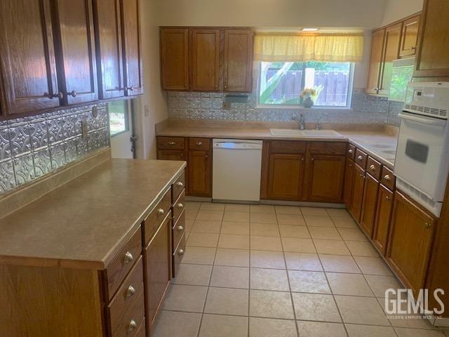 kitchen featuring white appliances, light tile patterned floors, brown cabinetry, decorative backsplash, and a sink