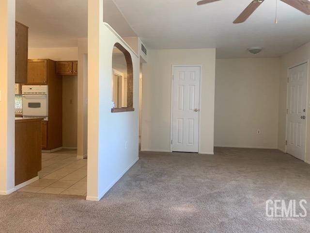 empty room with light carpet, ceiling fan, baseboards, and light tile patterned floors