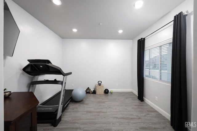 workout area featuring baseboards, light wood finished floors, and recessed lighting