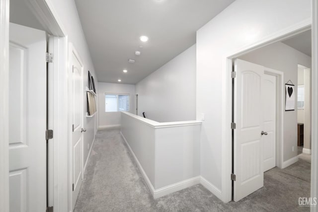 hallway with baseboards, light carpet, and an upstairs landing