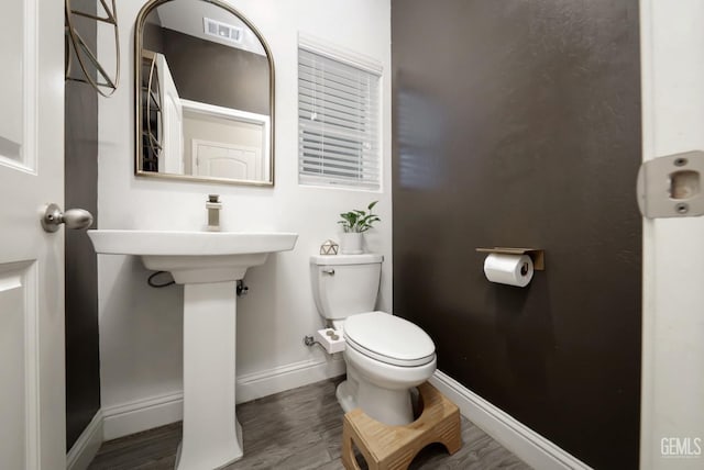 half bath with toilet, baseboards, visible vents, and wood finished floors