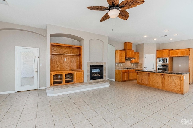 unfurnished living room with built in features, a ceiling fan, baseboards, light tile patterned floors, and a glass covered fireplace