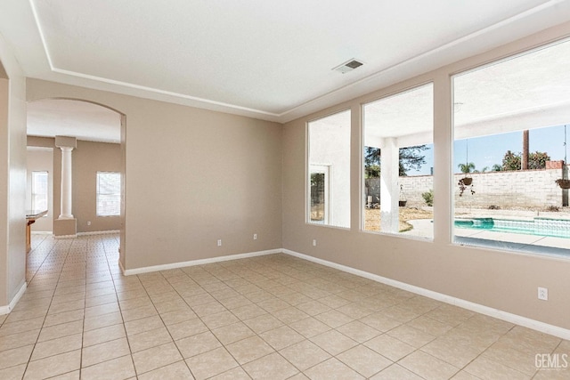 empty room featuring decorative columns, arched walkways, visible vents, and baseboards