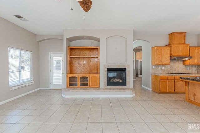 unfurnished living room featuring light tile patterned floors, a glass covered fireplace, ceiling fan, and baseboards