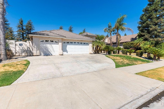 ranch-style house featuring a tiled roof, concrete driveway, stucco siding, an attached garage, and a gate