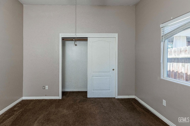 unfurnished bedroom featuring baseboards, dark colored carpet, and a closet