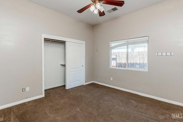 unfurnished bedroom with visible vents, a closet, dark colored carpet, baseboards, and ceiling fan