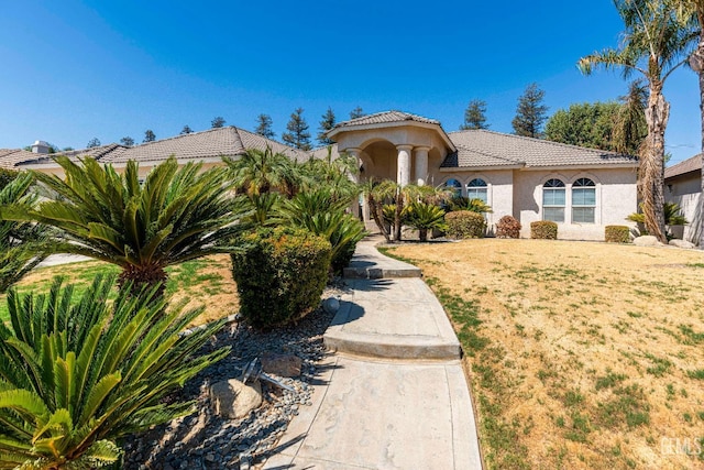 mediterranean / spanish-style house with a front yard, a tiled roof, and stucco siding