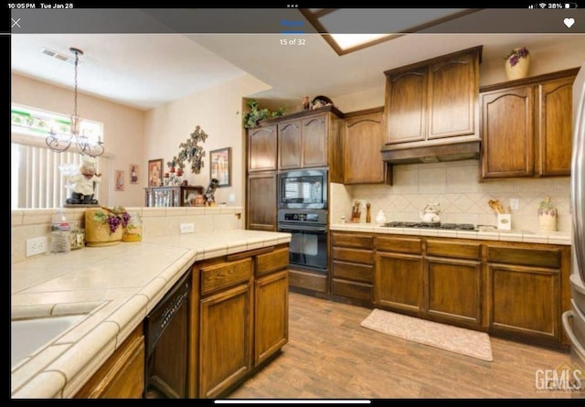 kitchen with decorative light fixtures, tasteful backsplash, tile counters, black appliances, and light wood-type flooring