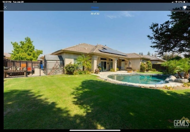 rear view of house with a fenced in pool, a lawn, and solar panels