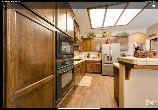 kitchen featuring tile countertops, black appliances, and light wood-type flooring