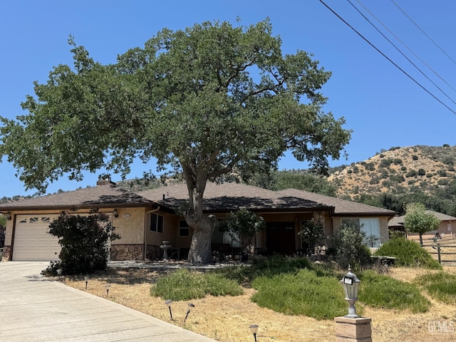 22417 Citation St, Tehachapi, CA 93561 - view of front of property featuring an attached garage, concrete driveway, stone siding, a mountain view, and stucco siding