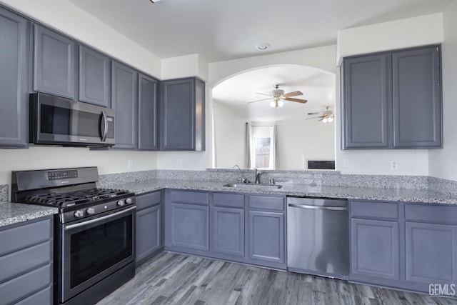 kitchen with stainless steel appliances, light stone countertops, sink, and light hardwood / wood-style floors