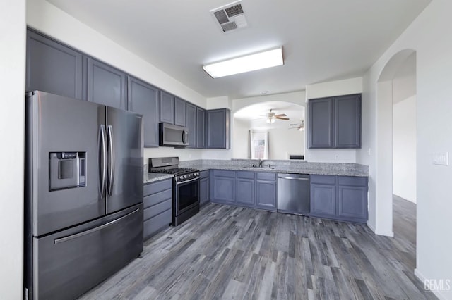 kitchen featuring appliances with stainless steel finishes, sink, hardwood / wood-style flooring, ceiling fan, and light stone counters