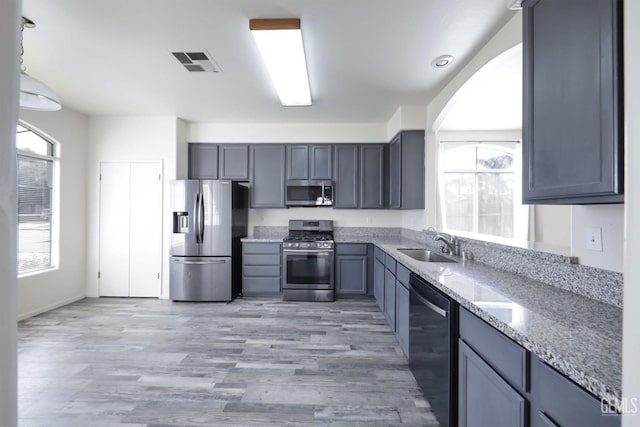 kitchen featuring sink, light stone counters, appliances with stainless steel finishes, gray cabinets, and light hardwood / wood-style floors