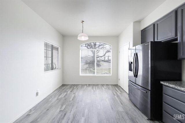 kitchen with gray cabinetry, stainless steel fridge, hanging light fixtures, light hardwood / wood-style floors, and light stone countertops