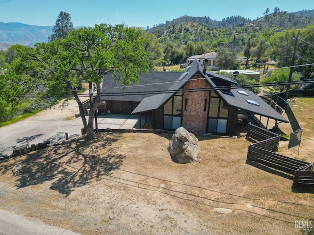 view of front of home featuring a shingled roof, a forest view, fence, a mountain view, and driveway