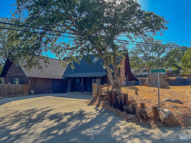 view of front of property with an attached garage, a shingled roof, concrete driveway, and fence
