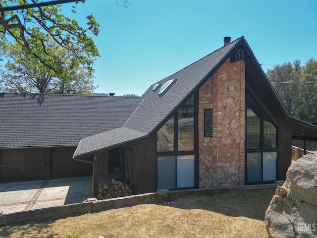 rear view of property with brick siding, driveway, and a shingled roof