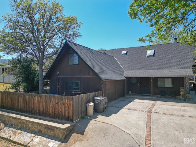 view of front facade featuring concrete driveway, an attached garage, fence, and a shingled roof