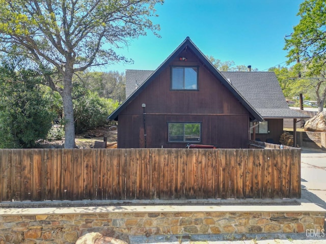view of side of property with fence and a shingled roof