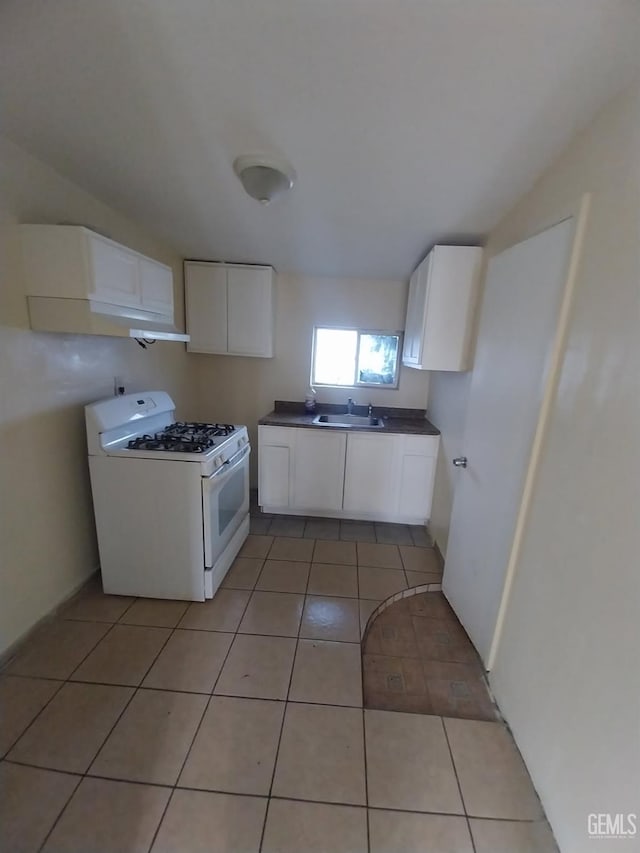 kitchen with light tile patterned floors, dark countertops, white gas stove, white cabinetry, and a sink