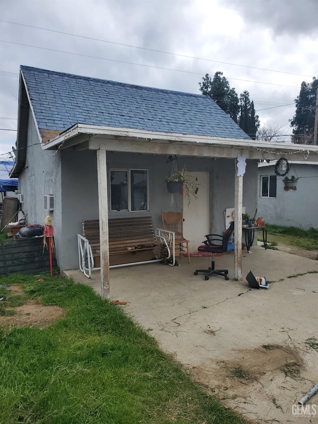 rear view of house featuring a patio area, a shingled roof, and stucco siding