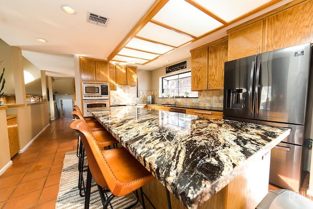 kitchen featuring stainless steel appliances, tasteful backsplash, visible vents, and brown cabinets