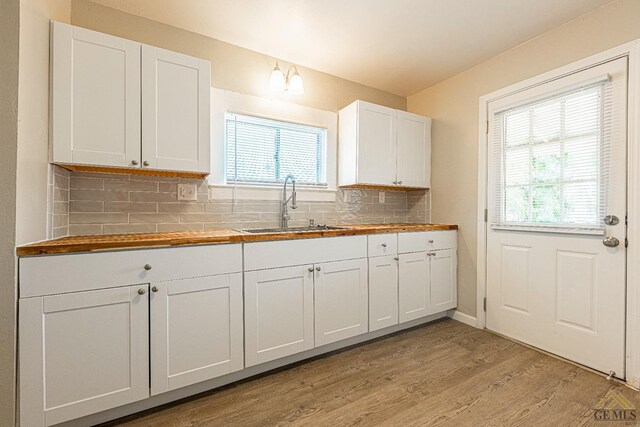kitchen featuring plenty of natural light, wooden counters, tasteful backsplash, light wood-type flooring, and a sink