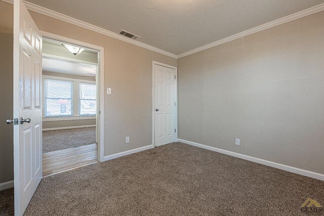 carpeted spare room featuring visible vents, baseboards, and crown molding