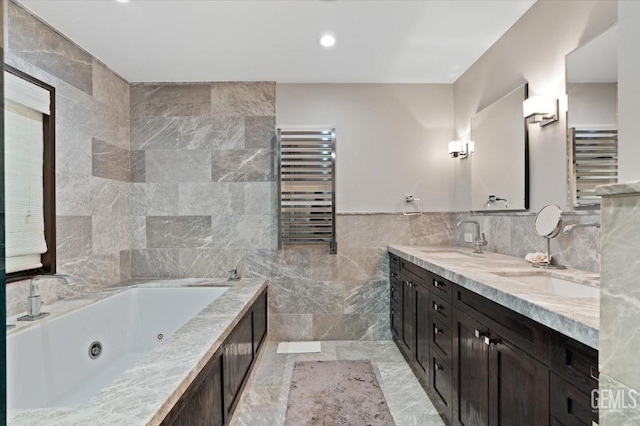 full bath with a sink, double vanity, radiator, a jetted tub, and tile walls