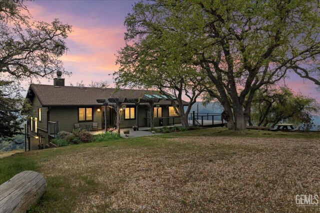 view of front of house featuring a pergola, a shingled roof, a front lawn, a chimney, and a patio