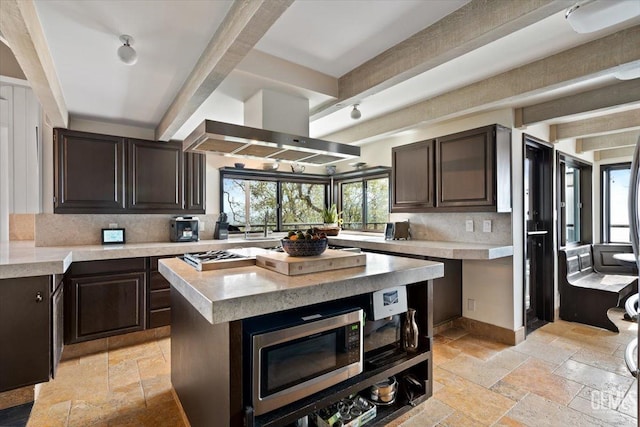 kitchen featuring stone tile floors, beam ceiling, wall chimney exhaust hood, and light countertops