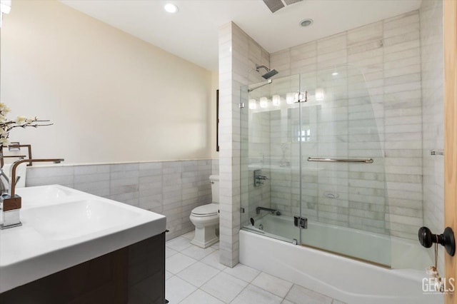 bathroom with tile patterned flooring, toilet, tile walls, a wainscoted wall, and enclosed tub / shower combo