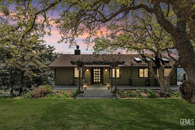 back of house at dusk featuring a lawn, french doors, a porch, and a chimney