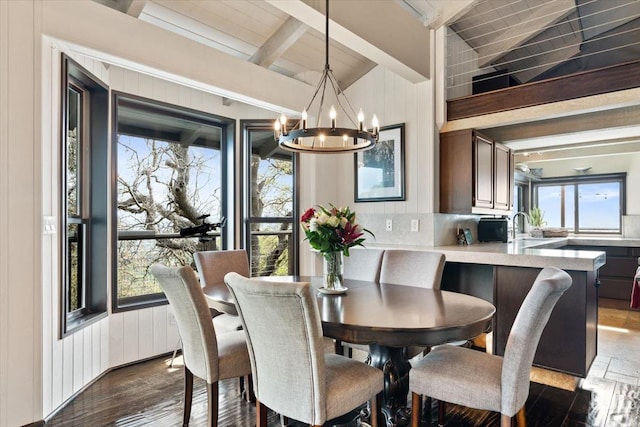 dining area featuring vaulted ceiling with beams, wood walls, dark wood-style flooring, and a chandelier