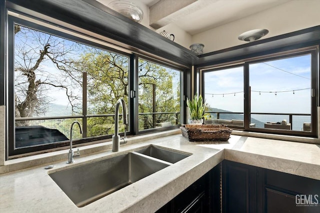 kitchen with a sink, light stone counters, dark cabinetry, and plenty of natural light