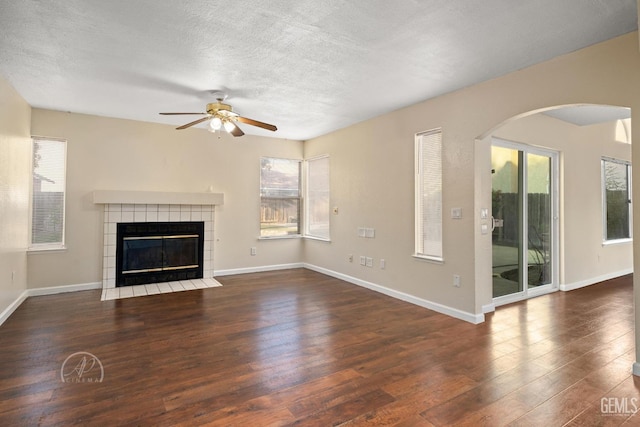 unfurnished living room featuring dark wood-type flooring, ceiling fan, a tiled fireplace, and a textured ceiling