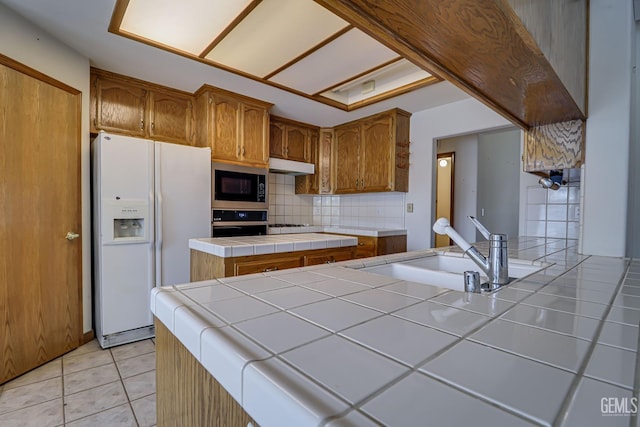 kitchen with built in microwave, tile counters, white fridge with ice dispenser, sink, and black oven