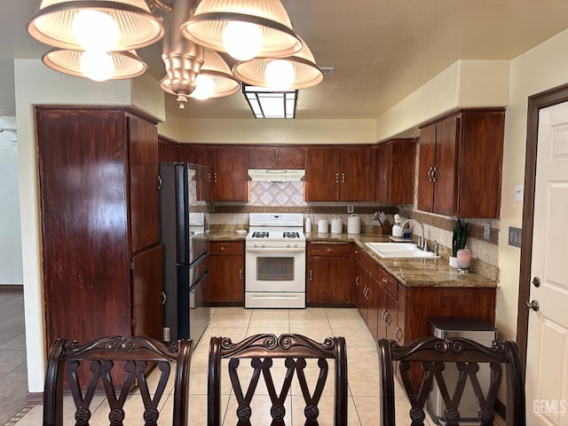 kitchen featuring tasteful backsplash, white gas stove, under cabinet range hood, and a sink