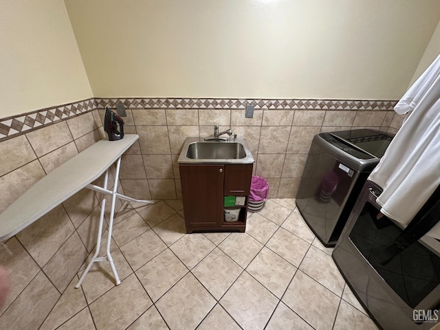 interior space featuring tile walls, washing machine and clothes dryer, laundry area, and a sink