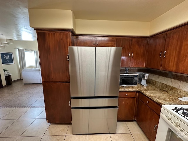 kitchen featuring light tile patterned flooring, light stone countertops, white range with gas cooktop, and freestanding refrigerator