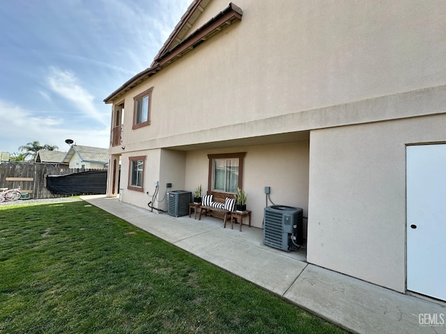 back of house with stucco siding, a yard, fence, a patio, and central AC unit
