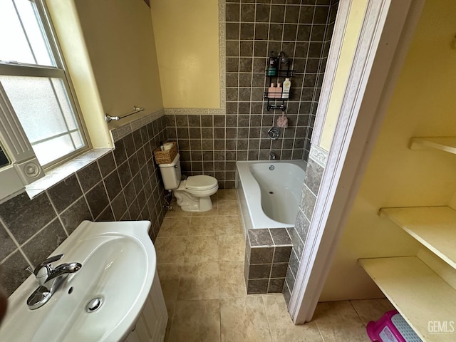 full bath with tile walls, a sink, toilet, tile patterned flooring, and wainscoting