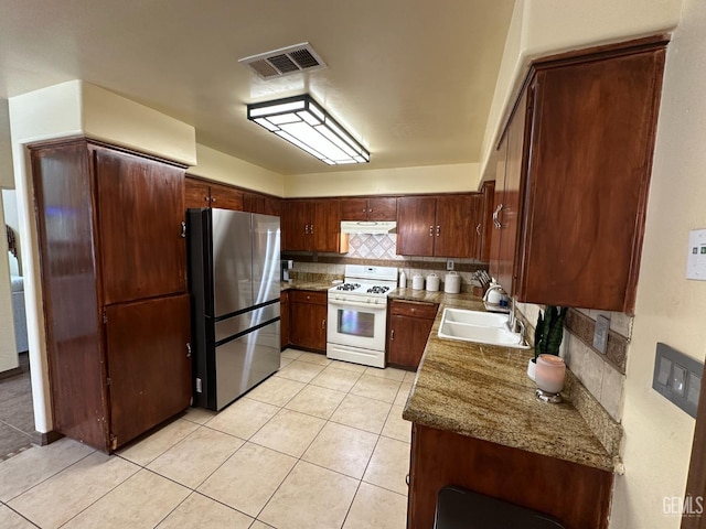 kitchen featuring freestanding refrigerator, white gas range oven, under cabinet range hood, a sink, and visible vents