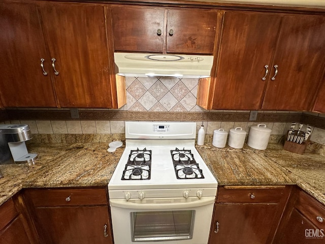 kitchen with white gas range, stone countertops, under cabinet range hood, and decorative backsplash