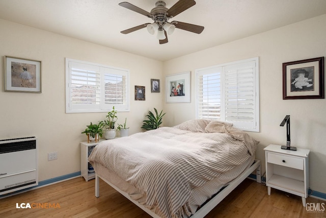 bedroom featuring multiple windows, hardwood / wood-style floors, heating unit, and ceiling fan