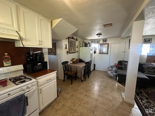 kitchen featuring a textured ceiling, light tile patterned floors, white cabinets, and white appliances