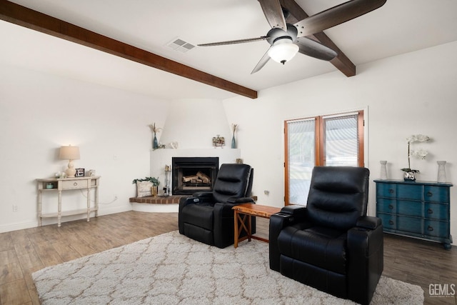 living room with beamed ceiling, a large fireplace, hardwood / wood-style floors, and ceiling fan