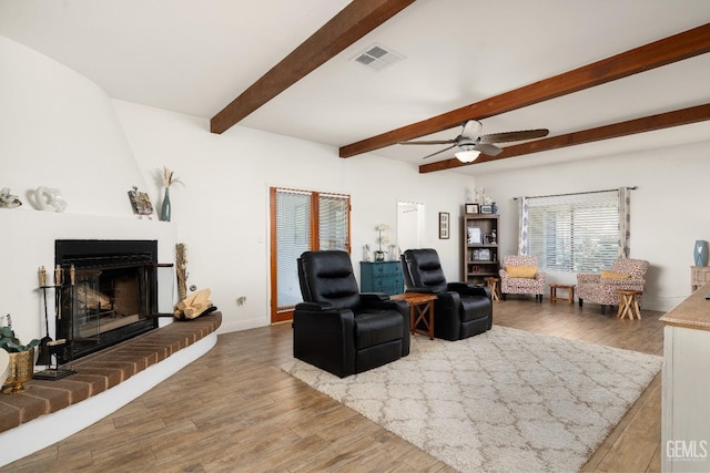 living room featuring ceiling fan, wood-type flooring, a fireplace, and beam ceiling